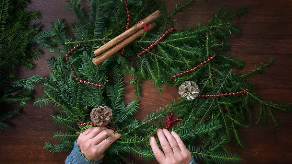Immergrüne Zweige werden mit Dekorationen für einen Adventskranz arrangiert. 